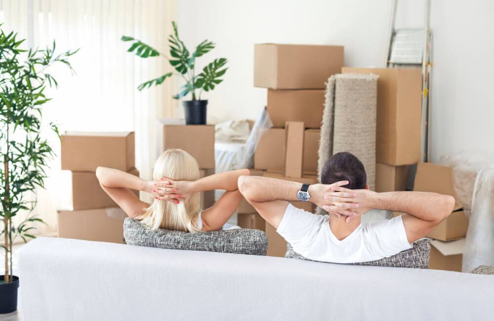 Un homme et une femme vus de dos et assis dans un canapé face à des cartons de déménagement